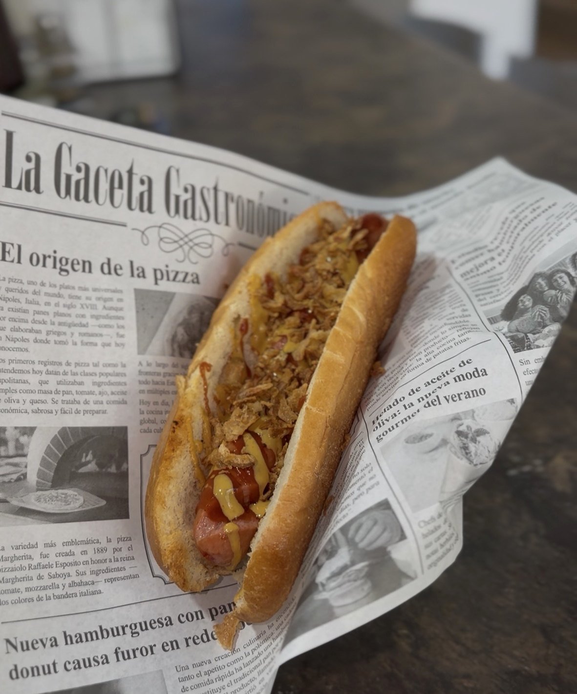 Frankfurt con cebolla crujiente, kétchup y mostaza servido en papel de periódico